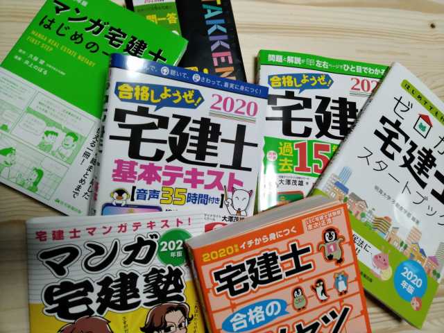 机の上に沢山の宅建士受験参考書を並べて、検討している様子の写真